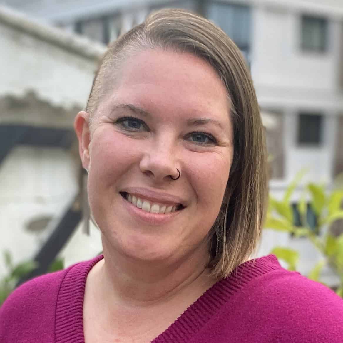 headshot of Kimberly on a balcony wearing a magenta sweater