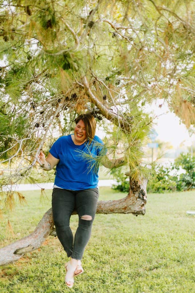 kimberly in a blue shirt sitting in a tree laughing