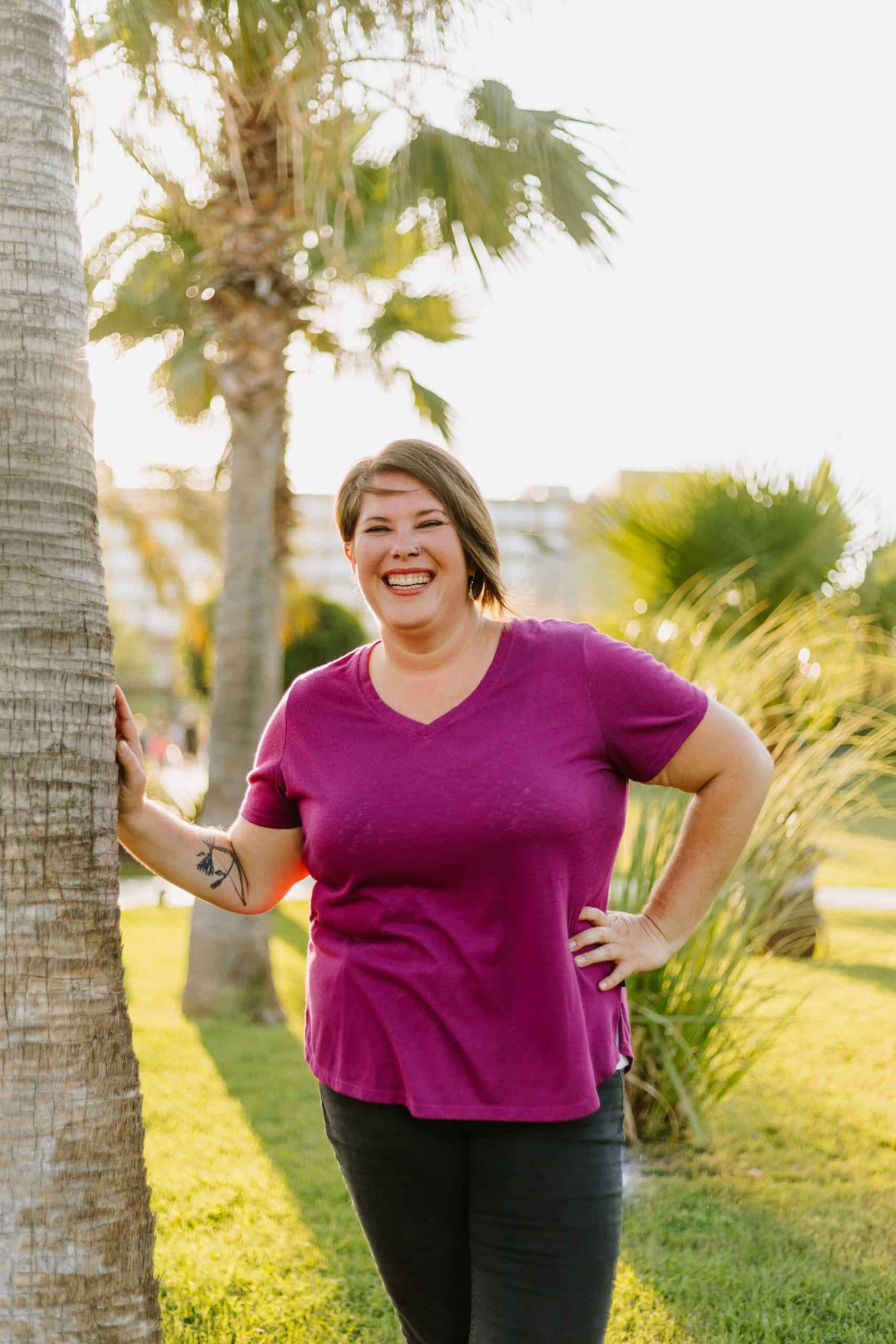 kimberly in a magenta shirt laughing by a tree as the sun sets